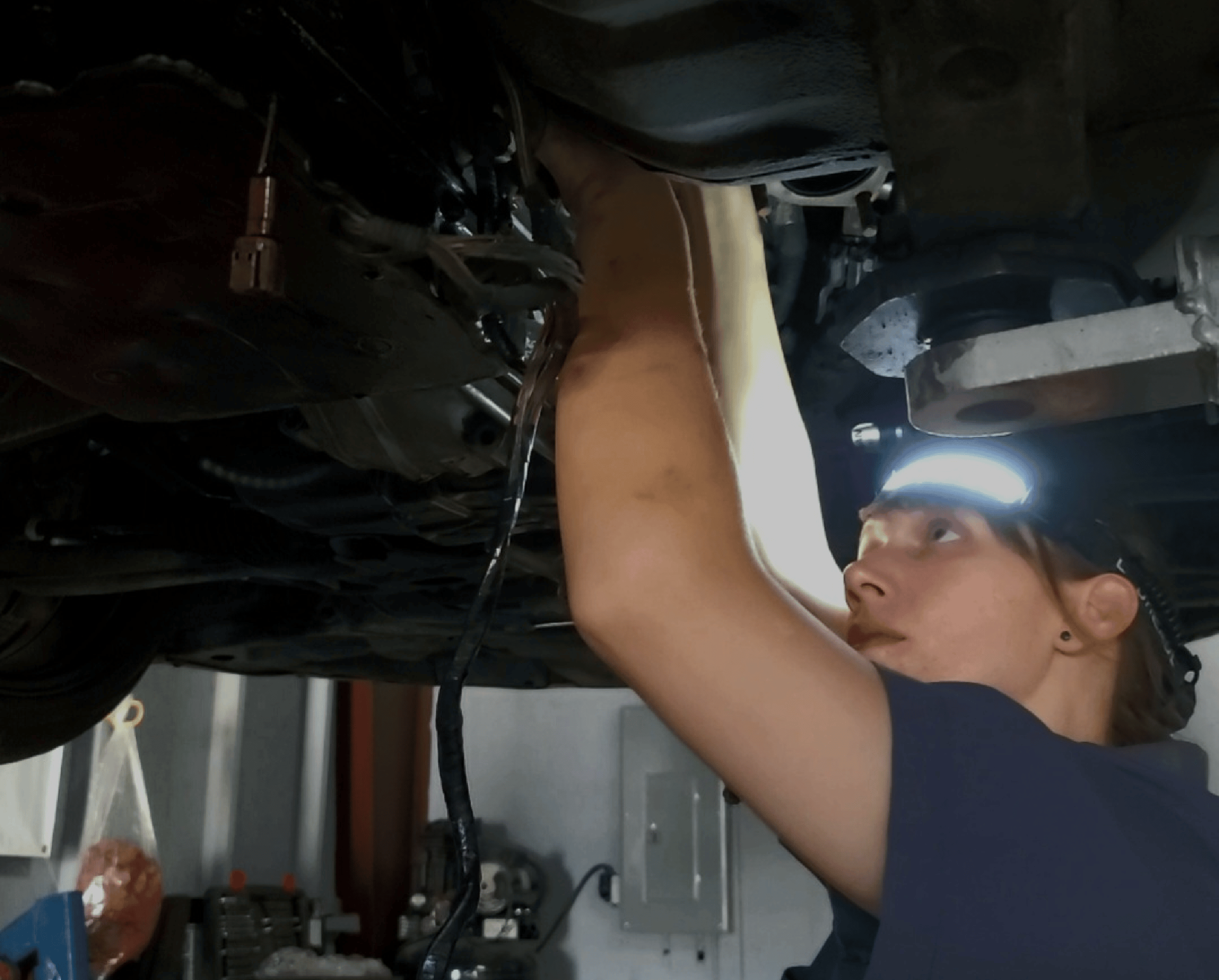 Image of auto shop owner Brittni Stangel checking the underside of a lifted car. Concept image of auto repair at Brittni's Automotive.