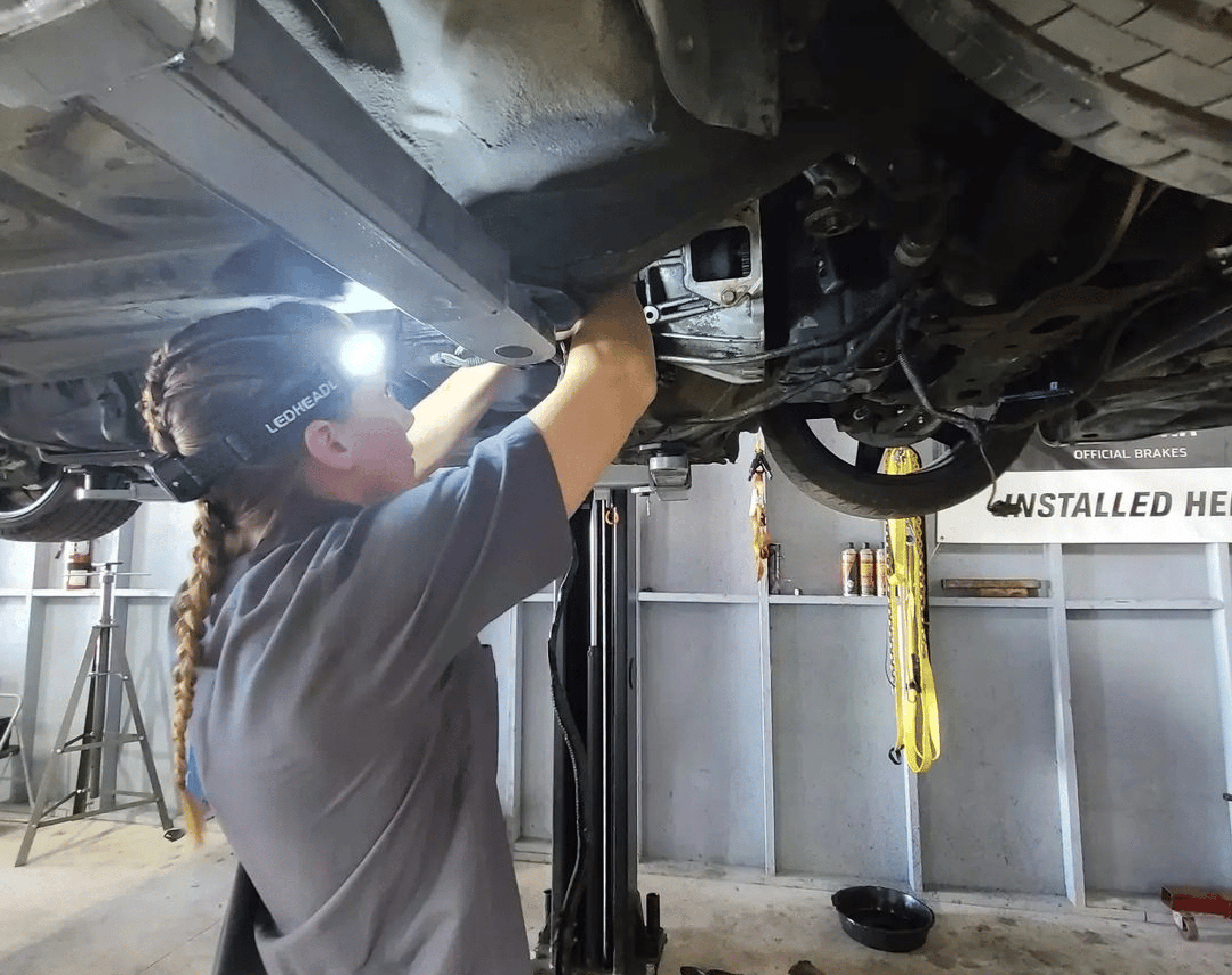 Image of auto shop owner Brittni Stangel checking the underside of a lifted car. Concept image of auto repair at Brittni's Automotive.